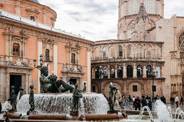 Naklejka premium Fuente del Turia fountain and tourists at Valencia Cathedral square with church and bell tower in background