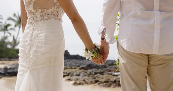 Middle aged Caucasian couple hold hands during wedding on white sand beach in Maui, Hawaii. Close up of arms and hands. 