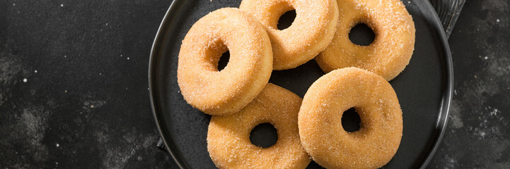Doughnuts in sugar on a black plate on the black kitchen table. Lots of doughnuts on the plate. Top view with a space for text. Banner