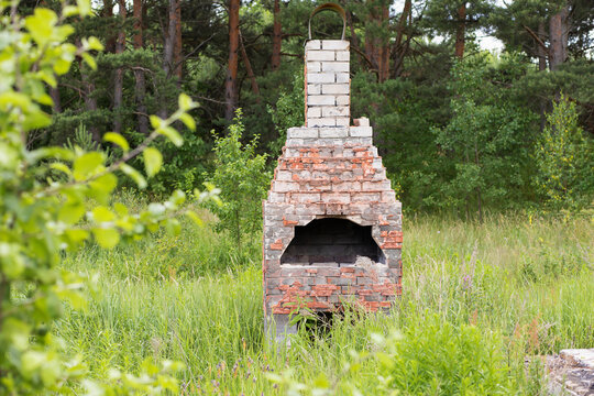 a red and white brick stove stands in nature among greenery