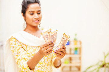 Indian woman wearing traditional ethnic clothes counting money over white background at home