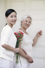 Senior woman knocking on a door, woman with a bouquet of flowers holding her hand