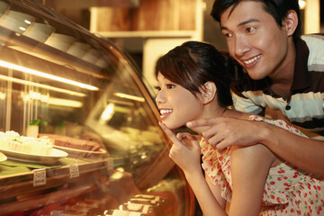Man and woman looking at the variation of cakes displayed in restaurant