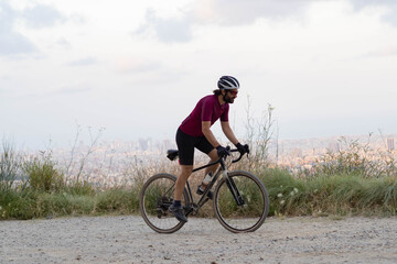 Cyclist man pedaling standing with his gravel bike with the city of Barcelona on the horizon