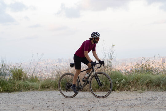 Cyclist man pedaling standing with his gravel bike with the city of Barcelona on the horizon