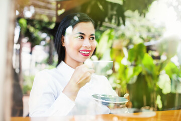 Young asian woman drinking coffee. View through the window