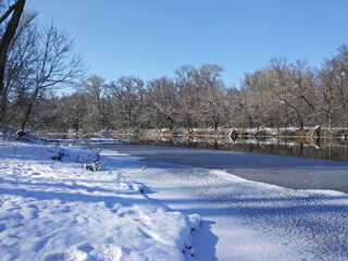 Sunny winter day on the river. The shore covered by snow and river covered by ice.