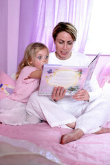 A woman sitting on the bed reading bedtime story for her excited daughter