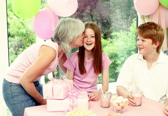 A woman giving her daughter a birthday kiss while her son watching