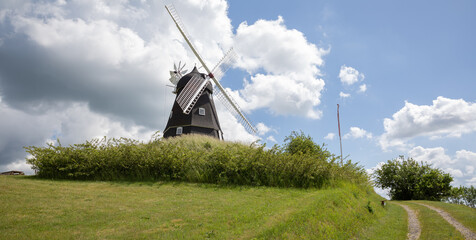 old mill sitting on top of the hill with blue sky and clouds 