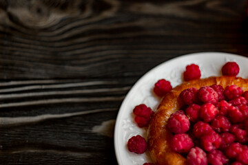 cheesecake with fresh raspberries on a white plate; dark background shot from above