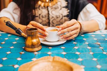 Closeup photo of woman holding a cup of turkish coffee in a cafe with turquoise tiles table