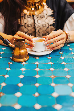 Closeup photo of woman holding a cup of turkish coffee in a cafe with turquoise tiles table