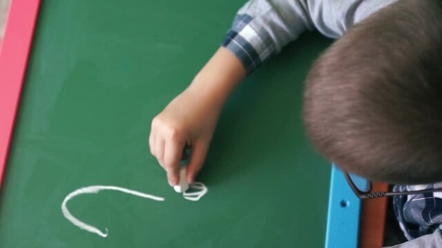 Concept on the topic of school education during quarantine. A boy in glasses 6-8 years old Caucasian writes a question mark on the blackboard with chalk. Pre-school education
