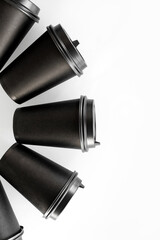 Pattern of black paper cups for tea or coffee on a white background. Recycling craft paper cups of coffee to go. Selective focus. Craft cup for hot beverage, takeaway. Disposable cup. Minimalist Style