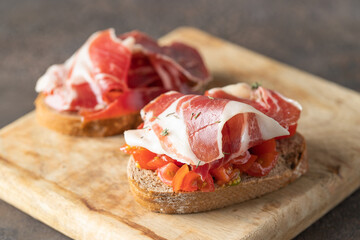 Crusty toast with fresh tomatoes and cured ham. Delicious appetiser Italian prosciutto and Spanish...