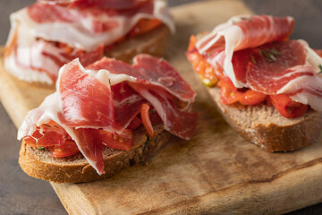 Wooden try with toasted brad slice with fresh tomatoes and cured ham. Delicious appetiser Italian...