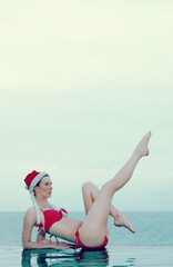 A Caucasian lady in red bikini sitting on the beach with one leg bended down and the other stretched up