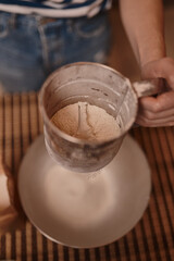 A young girl sifts the flour for making muffins. Cooks in the kitchen at home. Women's hands.
