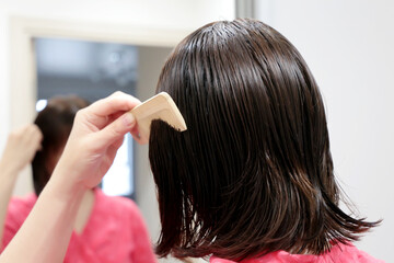Naklejka premium Woman combs her washed hair in front of a mirror. Grooming at home