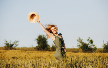 Happy woman jumping in wheat field holding hat in hand. The concept of freedom.