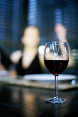 Focus on a glass of red wine with a woman in the background