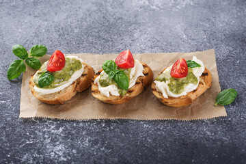 Bruschetta with mozzarella cheese, pesto, tomatoes and basil on gray texture background.