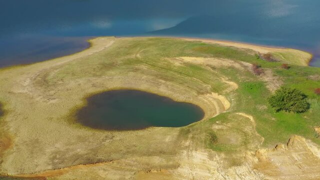 Island with pond in Rama Lake Bosnia and Herzegovina with eroded shore, Aerial flyover shot