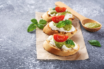 Bruschetta with mozzarella cheese, pesto, tomatoes and basil on gray texture background.