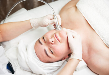 Woman relaxing while cosmetologist using massage device on her face