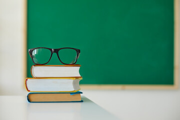 School education. Stack of books and teacher's glasses on desk at classroom. Pile of hardcover textbooks on table