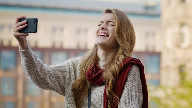 Happy girl pulling faces with phone outdoors. Laughing woman holding cellphone.