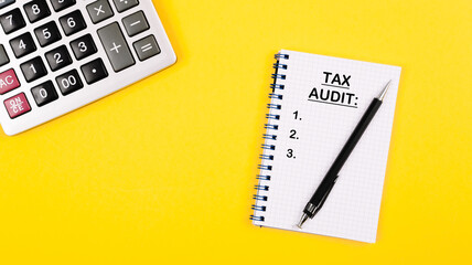 Tax audit written in black color as a list into the notepad. Accountant or auditor desktop layout with calculator and note with important day reminder. Positive yellow background.