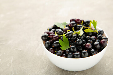 Black currant in a white bowl on grey concrete background