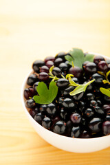 Black currant in a white bowl on wooden background