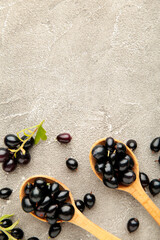 Black currant in wooden spoons on grey background