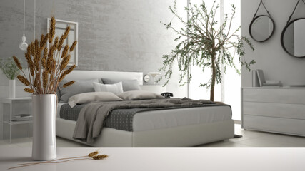 White table top or shelf with straws, dry plants, ornament, ears, sheaf, branch in vase, over gray and white bedroom with double bed, modern minimal interior design