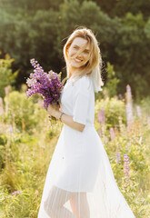 Lovely cute woman in lupine field, sunny day, freedom concept