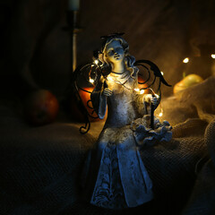 sculpture of a sitting angel against a burning candle and yellow garlands in the dark