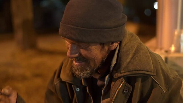 Passerby talking to homeless man on the sidewalk at night.