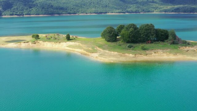 Small island with tree group in Rama Lake Bosnia and Herzegovina, Aerial flyover shot