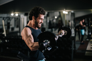 Fototapeta na wymiar Side view of sportive bearded young man with muscular wiry body wearing sportswear working out with barbell during sport workout training in modern dark gym. Concept of healthy lifestyle.