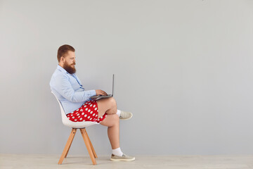 Funny fat man in a blue shirt and red shorts sitting on a chair working online using a laptop on a...