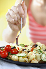Woman enjoying a plate of fruit and vegetable pasta salad served with feta cheese and olives on the side