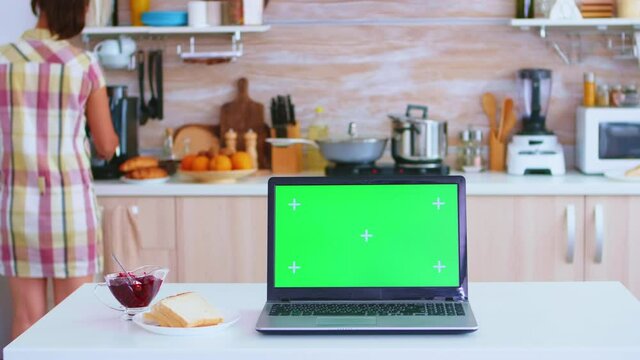 Laptop with green screen with kitchen and woman holding plate with tasty french croissants and a cup of coffee. Green screen chroma mock up isolated mockup background ready to be replaced with your