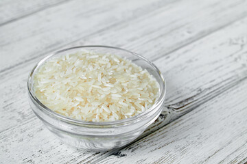 Raw white rice grains in a transparent glass plate on wooden background. Closeup
