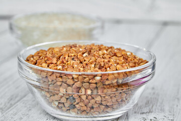 Raw white rice and buckwheat groats in a transparent glass plate on wooden background. Closeup