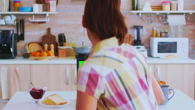 Woman looking at laptop with green mock up while drinking coffee in kitchen. Tasty french pastry. Green screen chroma mock up isolated mockup background ready to be replaced with your text, logo or