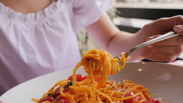 Closeup woman eat pasta in italian cuisine restaurant spinning spaghetti on a fork beautiful dish layout with tomatoes and basil