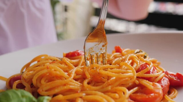 Closeup woman eat pasta in italian cuisine restaurant spinning spaghetti on a fork beautiful dish layout with tomatoes and basil